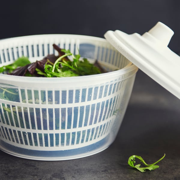 An UPPFYLLD salad spinner in white with the lid placed balanced on the side, the item is full of mixed salad.