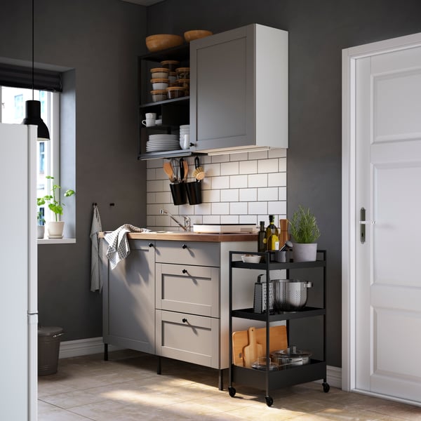 Una cocina amoblada con muebles grises y blancos. Sobre el mesón principal hay un mueble de muro y en su parte inferior una luz integrada que ilumina el mesón.