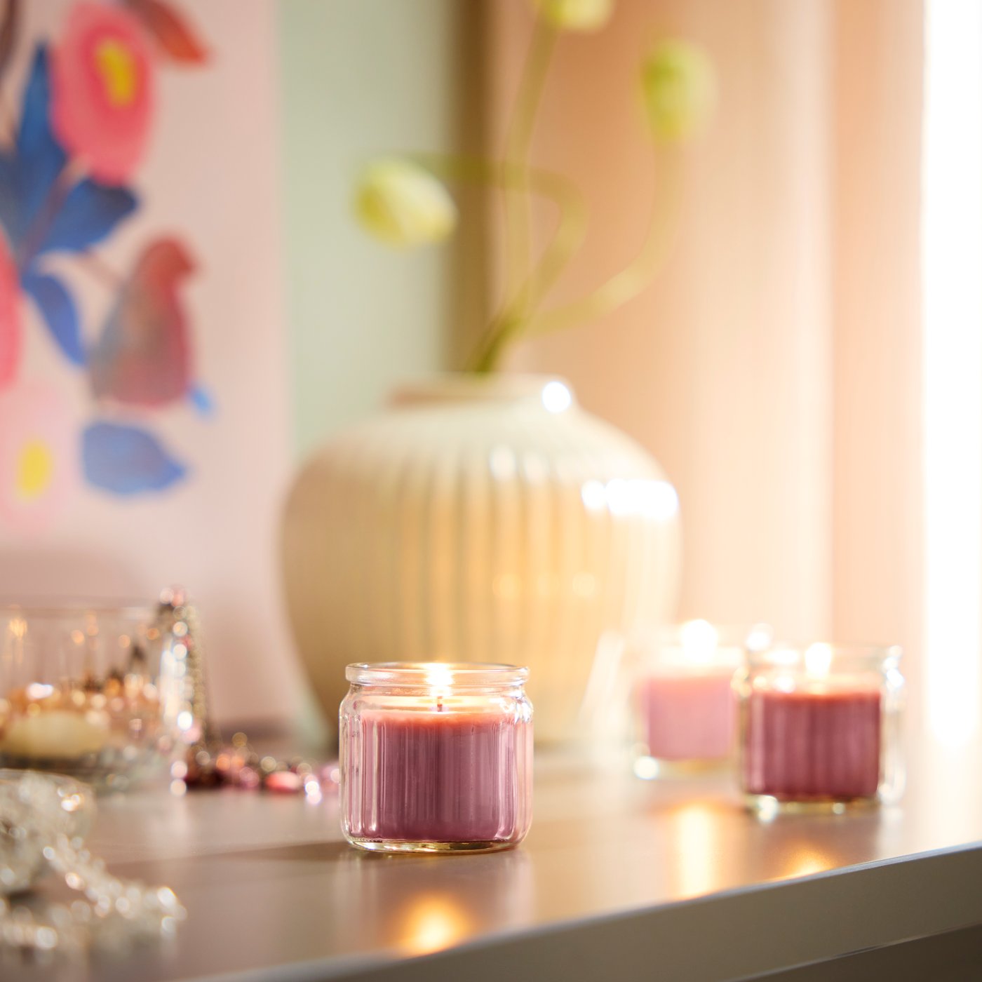 A pink scented candle stands on a light-colored table.