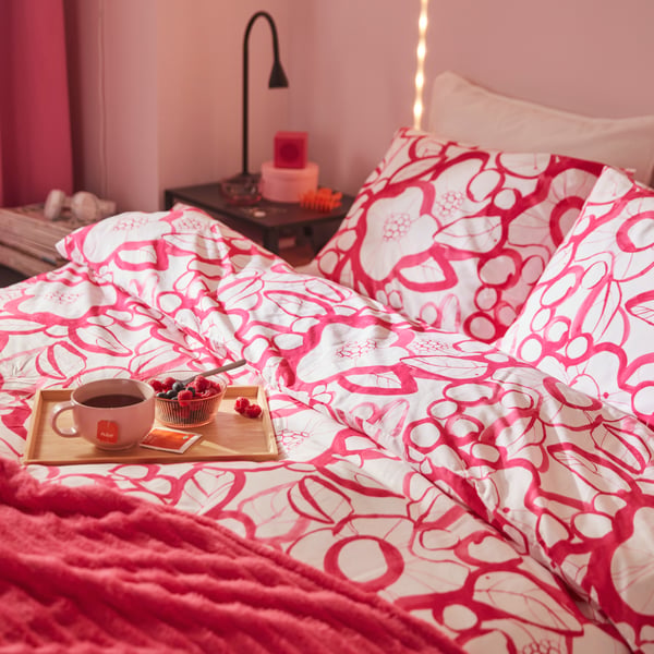 A bed with a white and bright pink floral HÄRLIR duvet cover and pillowcase and a bright pink GULLSTRÅLE bedspread.