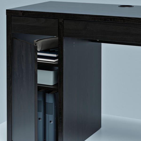 A section of a MICKE desk with a cabinet at one end, its door ajar, revealing neatly arranged binders and accessories.