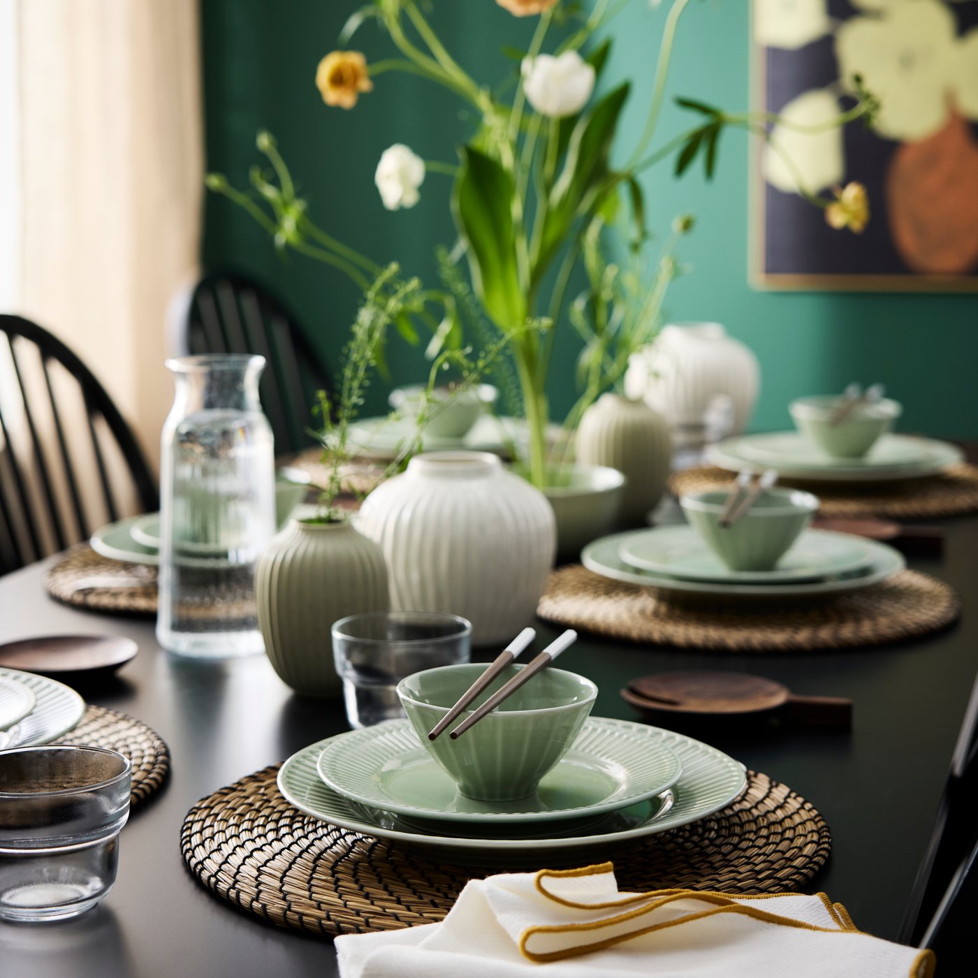 A dining table is set with pale grey-green STRIMMIG bowls, plates and side plates, chopsticks, glasses and flowers.