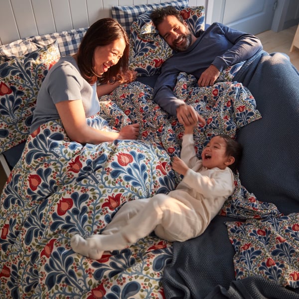 A family laughing in a bed with a floral multicoloured SÄTERVIDE duvet cover set in orange and blue.