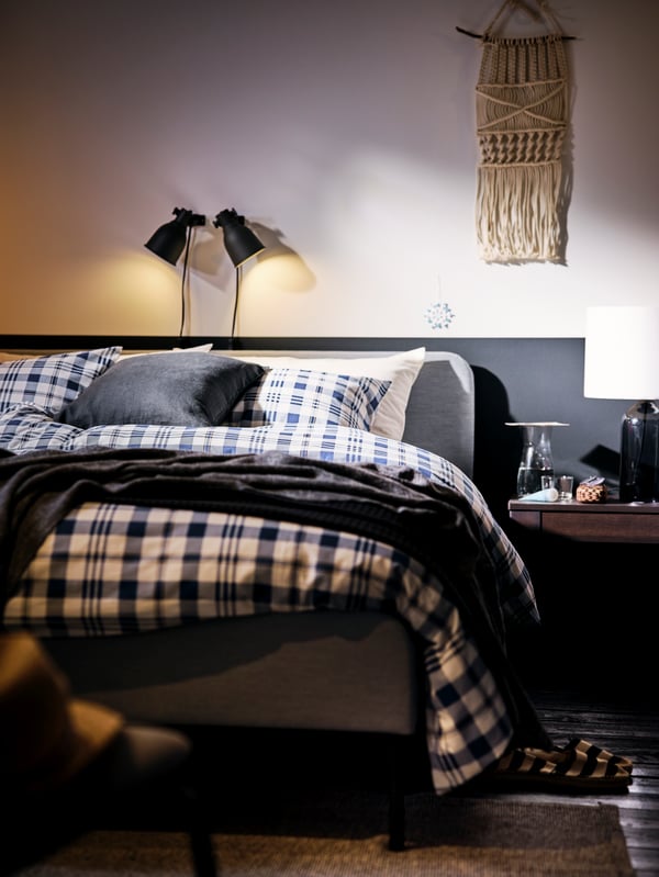 Un lit matelassé SLATTUM gris clair présenté ici avec du linge de lit SPIKVALLMO et éclairé par des appliques HEKTAR gris foncé.