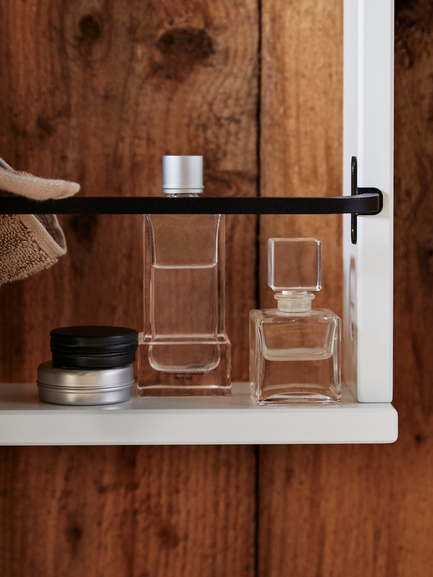 A white HEMNES shelf with two bottles of perfume and two metal canisters. A brown towel thrown over a black rail.