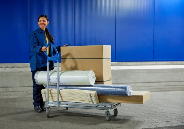 An IKEA co-worker pushing a flat trolley full of flatpack furniture.