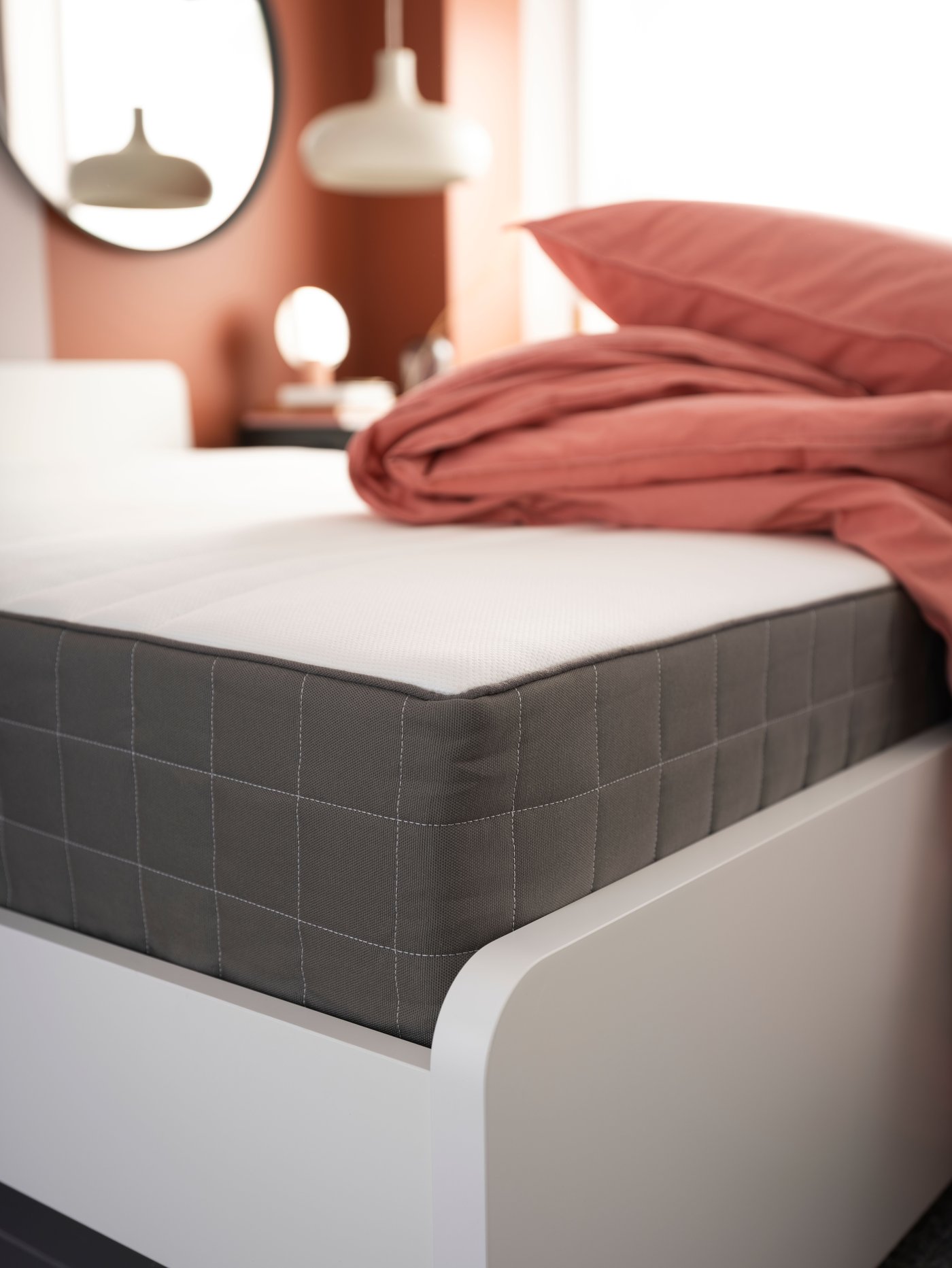 A HAUGESUND spring mattress on a white bed frame with a duvet cover and pillow folded in a pile on top.