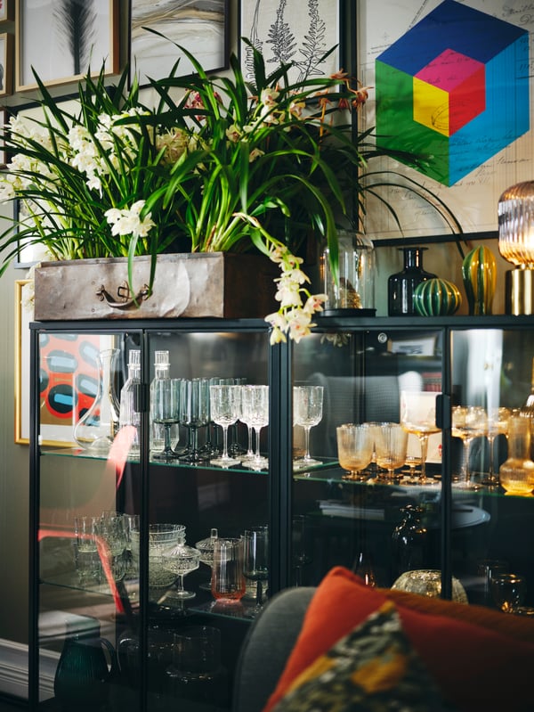Framed BILD posters on a wall above two anthracite RUDSTA glass-door cabinets filled with glassware with vases on top.