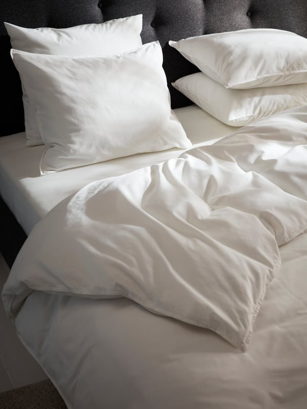 A dark grey IDANÄS upholstered bed with a duvet and four pillows dressed in white ÄNGSLILJA bed linen.