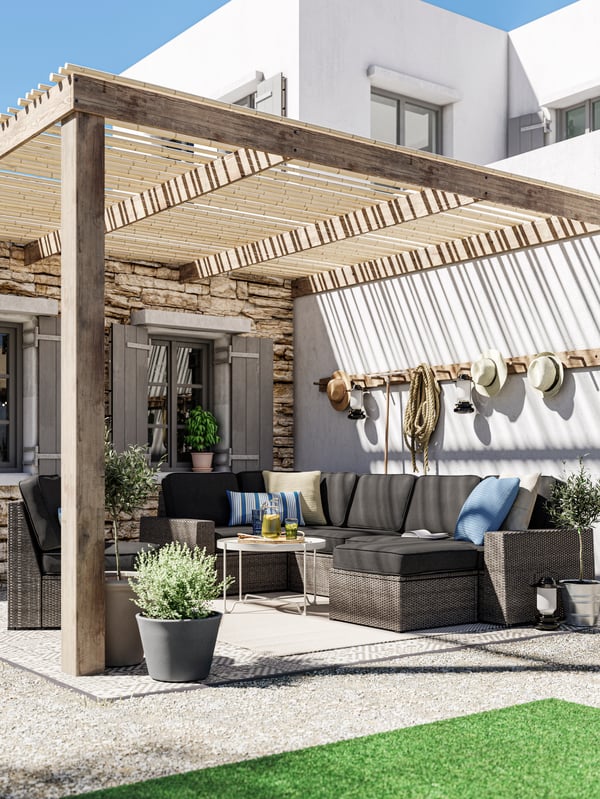 A lounge area with a dark grey outdoor sofa with anthracite cushions, a beige coffee table, decking and potted plants.