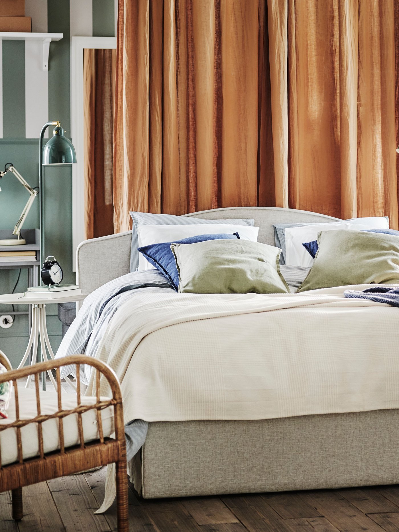 A bedroom with a RAMNEFJÄLL upholstered bed with a soft curved headboard in beige and soft rusty coloured linen curtains draping in the back.