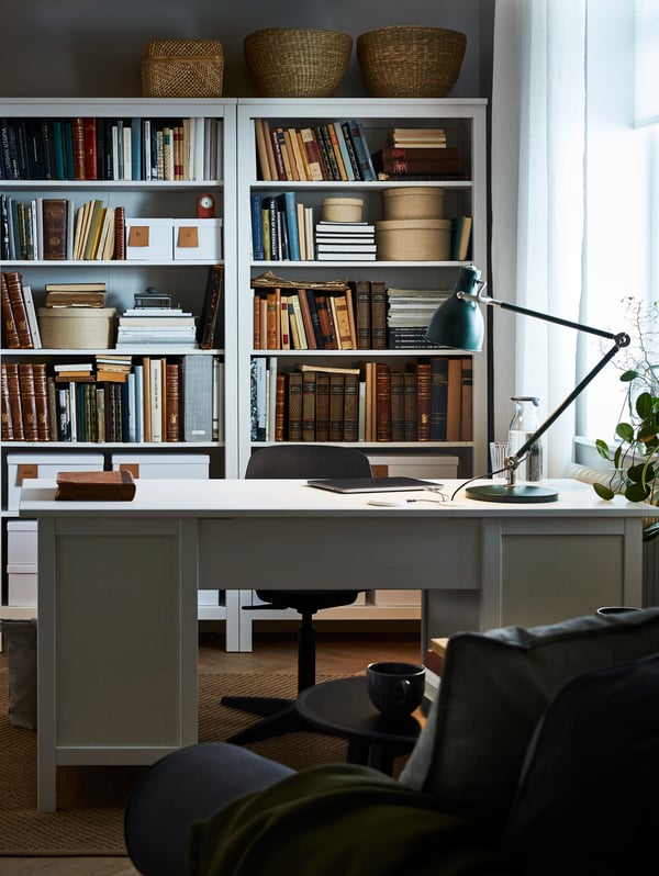 Room with white HEMNES desk and matching bookcases accessibly placed behind it with books, boxes and decorative storage.