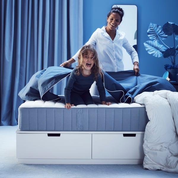 Hellblaue VALEVÅG‑Taschenfederkernmatratze (fest) auf weißem Bett in einem blau gestalteten Schlafzimmer.