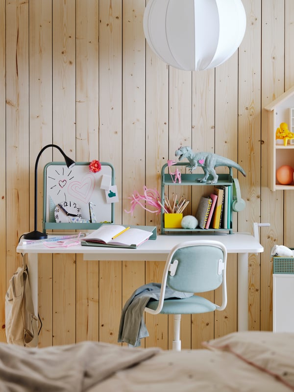 Children’s room with white desk and green and white chair, green writing board, bookshelf and whiteboard against wood wall.