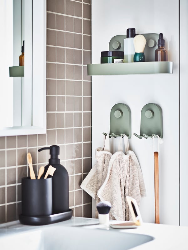 El costado de un lavamanos con un set de baño GANSJÖN. Al costado unas repisas con ventosas ÖBONÄS sosteniendo artículos de maquillaje.