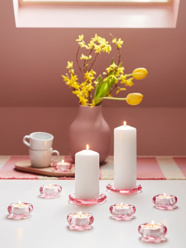Ein Tisch mit rosa Teelichthaltern, rosa Vase und zwei weiße Tassen.