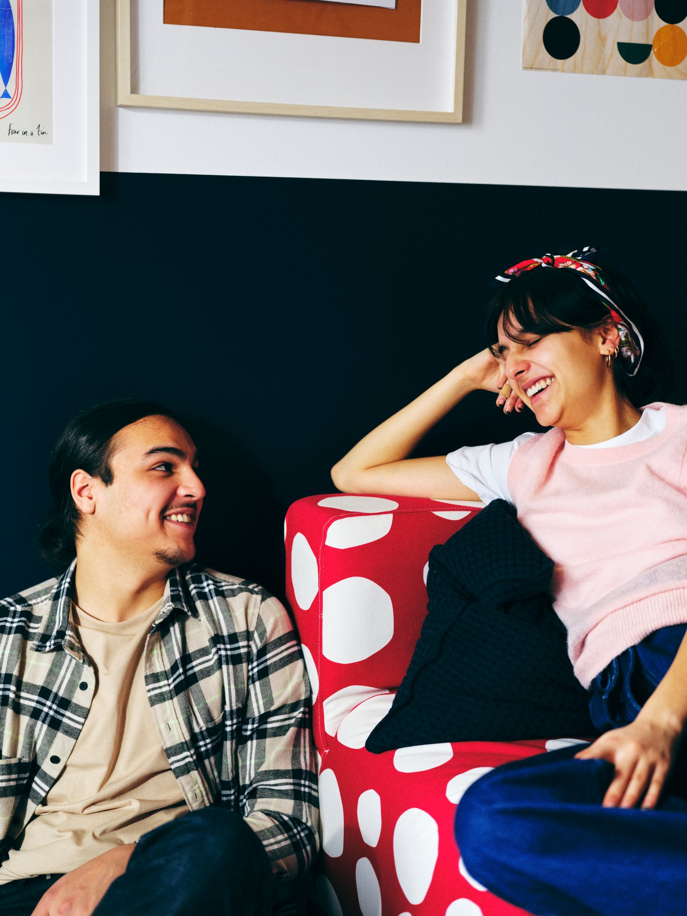 Un homme et une femme se sourient, elle est assise sur un canapé deux places KLIPPAN rouge/blanc, il sur le sol à côté.