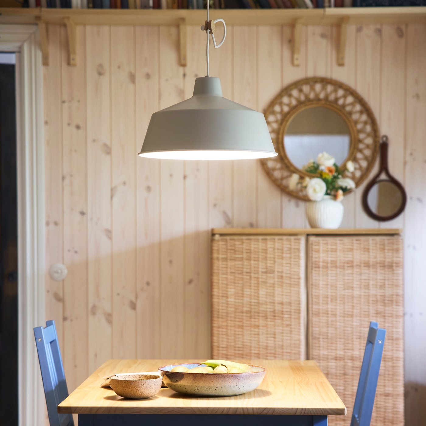 En SJÖMAKT pendellampa lyser upp ett PINNTORP bord med en GLADELIG serveringsskål och en skål ovanpå.