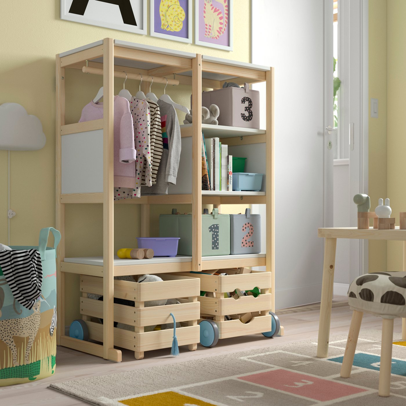 Wooden kids’ wardrobe organizer with hanging storage, cubby shelves, and pull-out bins in a bright playroom.
