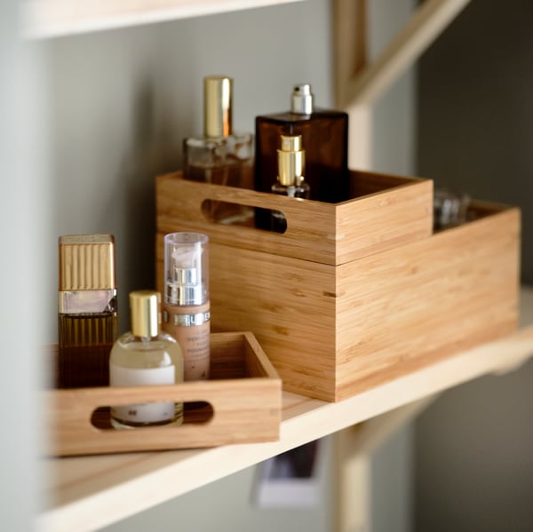 Petites boîtes en bambou sur une étagère murale en bois contentant des bouteilles de parfums et cosmétiques