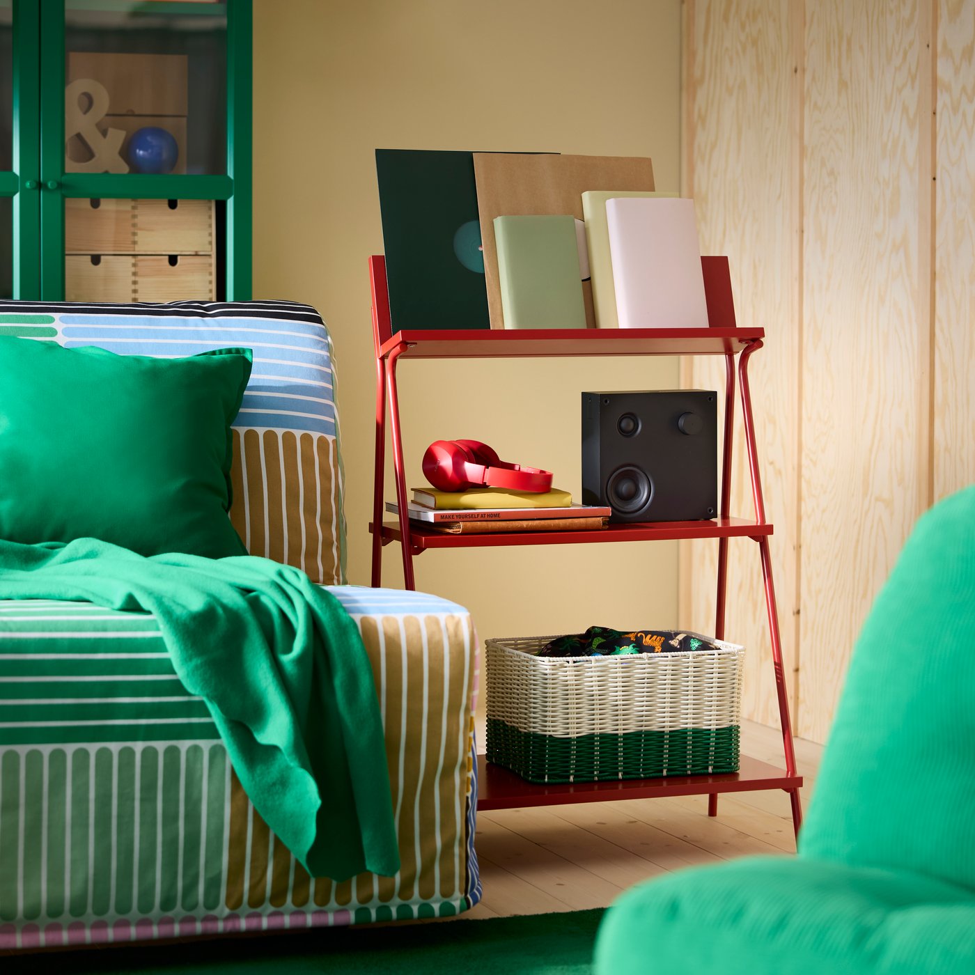 Freestanding red shelves beside sofa-bed with multi-coloured cover and green blanket.