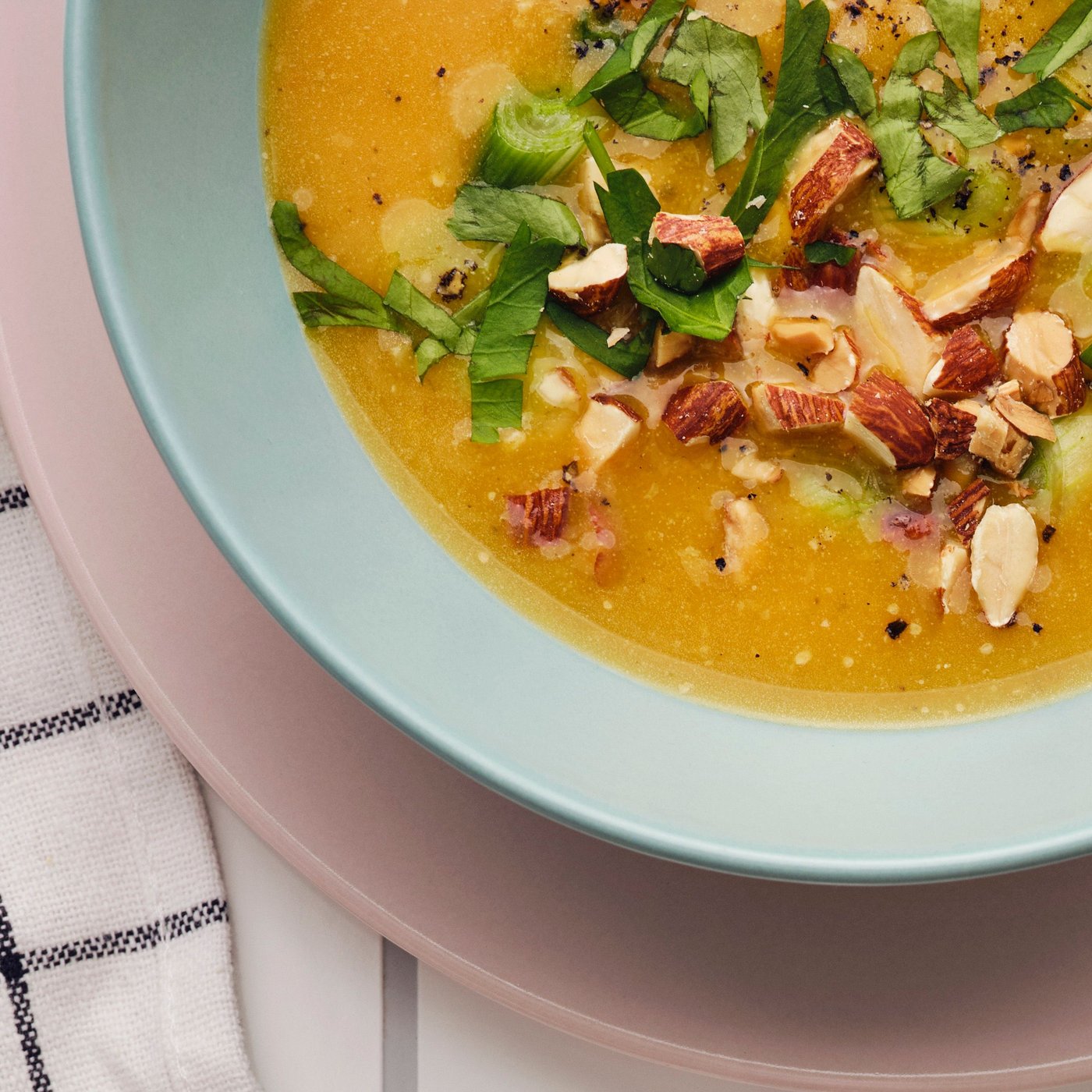 Græskarsuppe med krydderurter og MUNSBIT ristede mandler serveret i en blå skål ovenpå en lyserød tallerken.