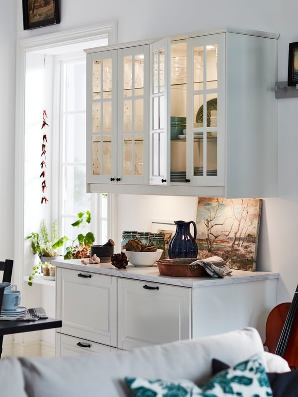 Two elegant off-white base cabinets with drawers under two traditional wall cabinets with glass doors and lighting.
