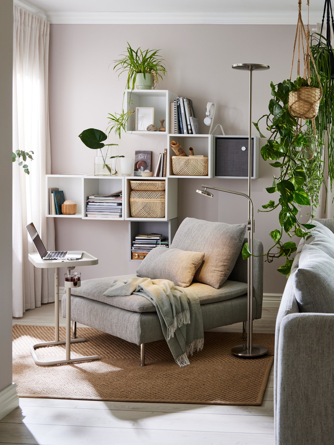A grey SÖDERHAMN seat section with a green throw in a corner by a window. A laptop stand with a laptop on is in front.