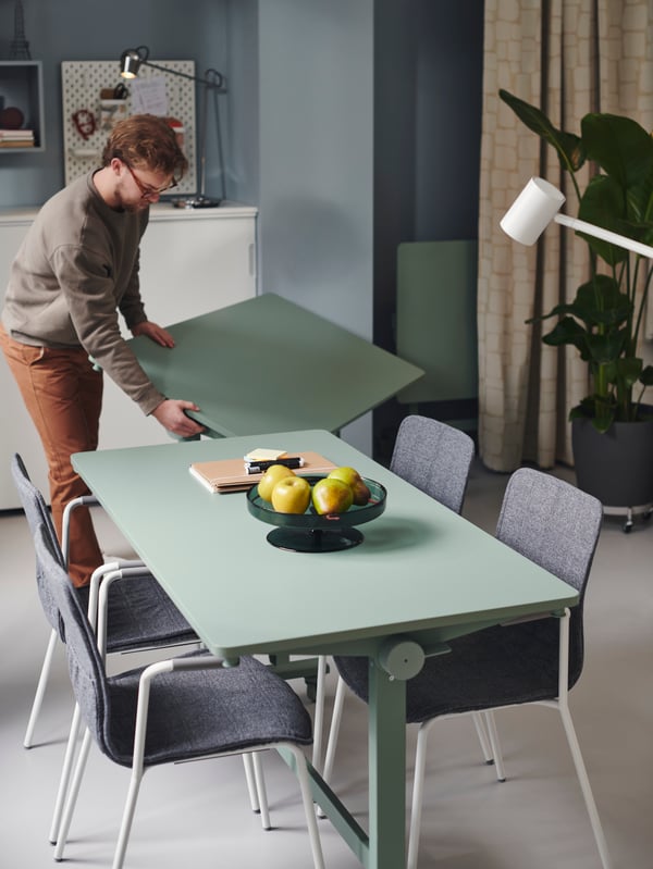 An office setup with MITTZON foldable table with castors and LÄKTARE conference chairs. A person is adding another table.