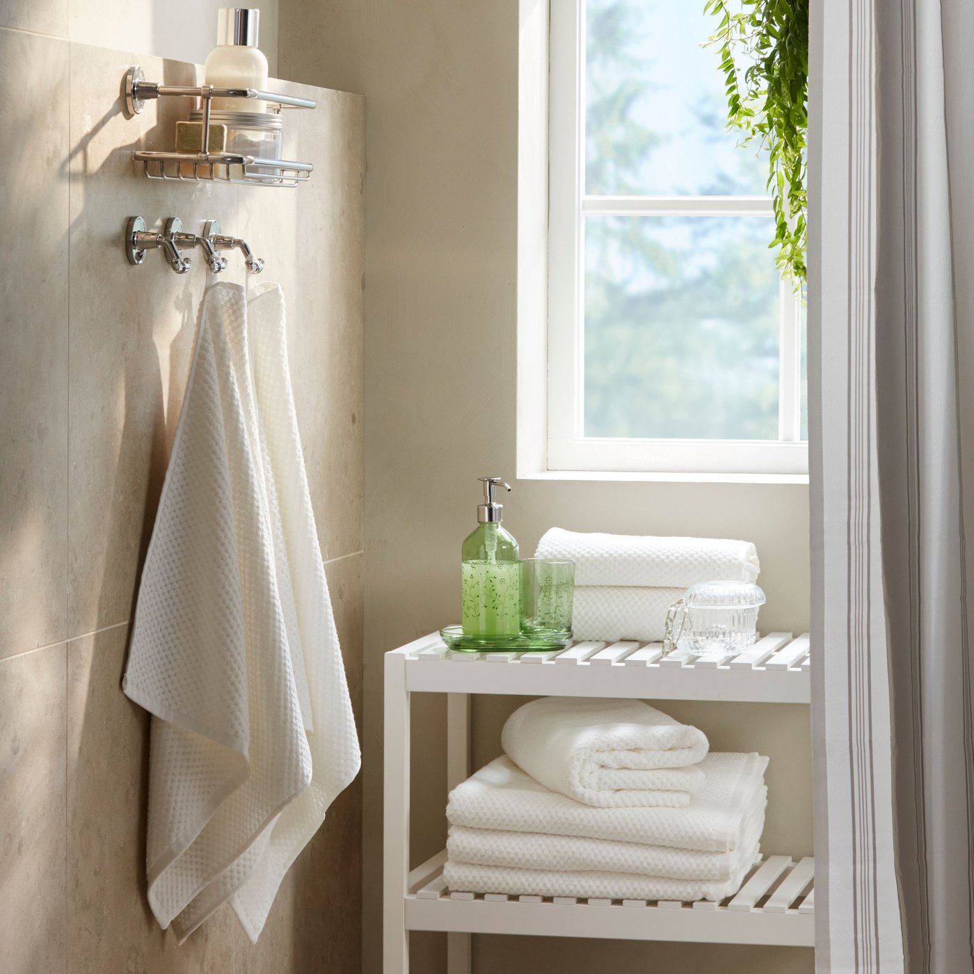 A bathroom corner has two white GULVIAL hand towels hanging on wall hooks by a white bench with stacked white towels.