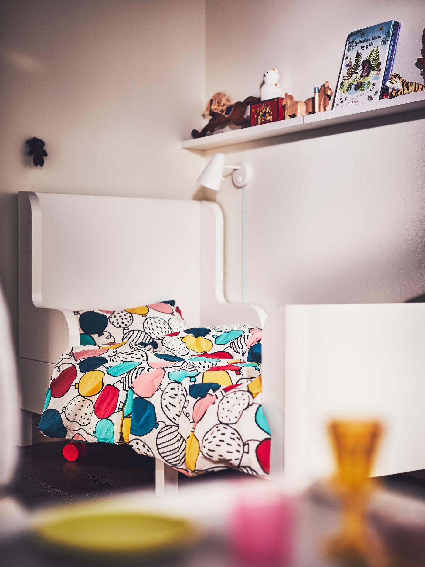 A children’s bedroom with a white BUSUNGE extendable bed covered in a multicolour BUSENKEL duvet cover and pillowcase.