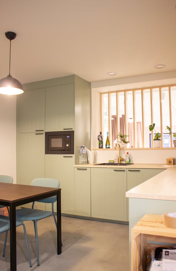 Een lichte, moderne keuken met pastelgroene kasten, een kookeiland, hoge krukken, houten accenten en zachte verlichting.