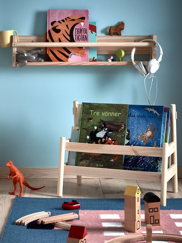 A FLISAT wall storage and book display holding books and toys in a blue child’s room with an UPPTÅG rug with toys on it.