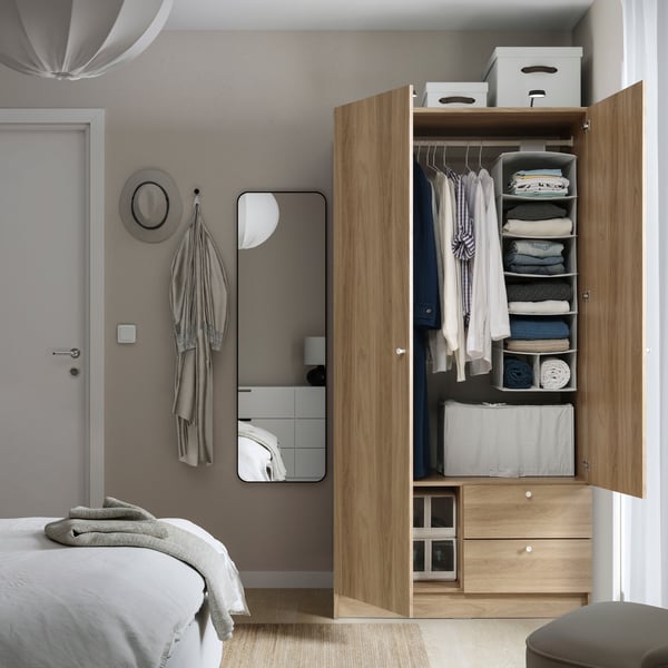 An oak-effect VILHATTEN wardrobe with 2 doors and drawers in a light bedroom with the doors open and a mirror on wall by it.