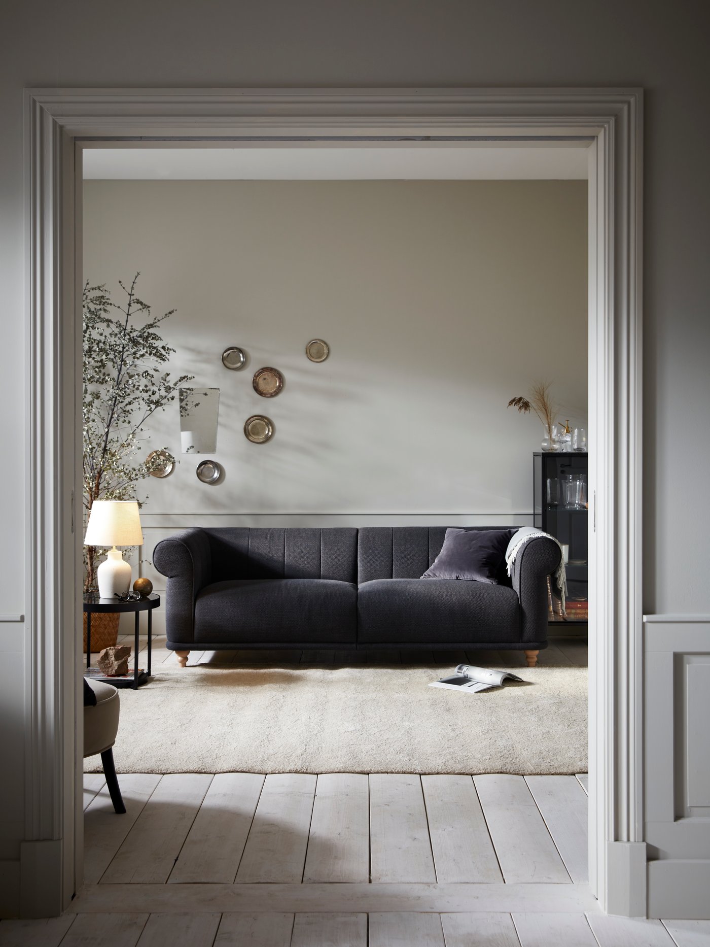 In einem Wohnzimmer steht ein VISKAFORS 3er-Sofa. Über eine Armlehne ist ein HOLMVI Plaid drapiert. Neben dem Sofa ist eine eingeschaltete Tischleuchte auf einem Beistelltisch zu sehen.