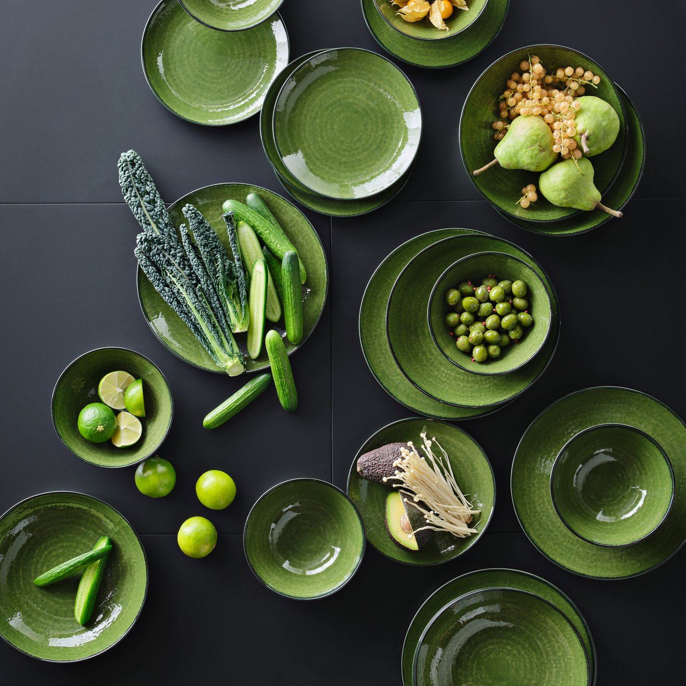 Gröna PELARKAKTUS skålar och tallrikar arrangerade med färska frukter och grönsaker som päron, lime, gurka och kål på en mörk yta.