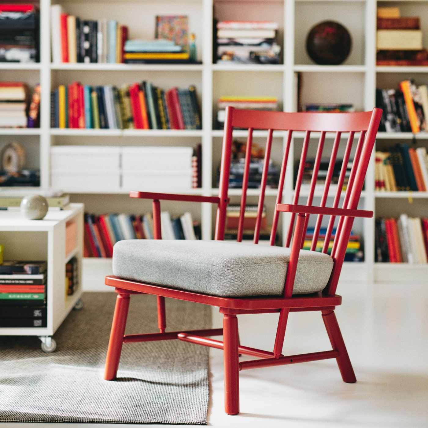 A brown-red PERSBOL armchair with a light grey chair pad in a living room with bookcases filled with books behind it.