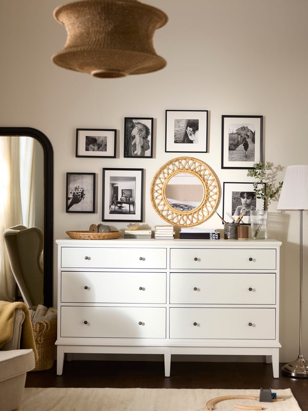 White IDANÄS chest of 6 drawers with decorations on top and lots of framed photos and a mirror on the wall above.