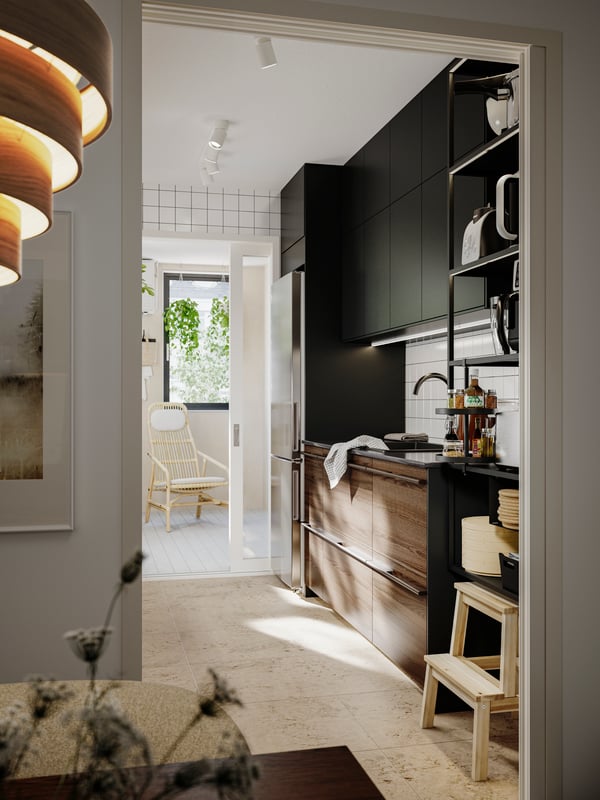 A kitchen with STENSTA dark brown ash veneer and black kitchen fronts with a stainless steel fridge and open shelving.