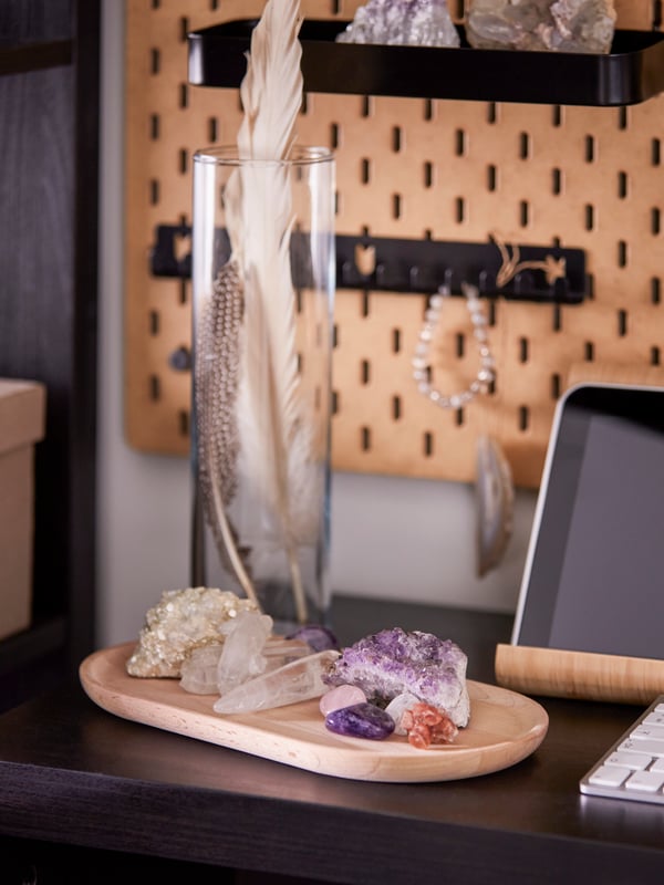 Crystals in different colours on a SMÖRLING serving tray made from solid beech wood next to a glass vase with feathers.