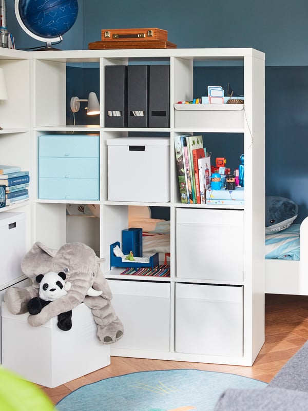 Two shelving units serve as a room divider while offering much storage space. Behind them, a children’s bed.