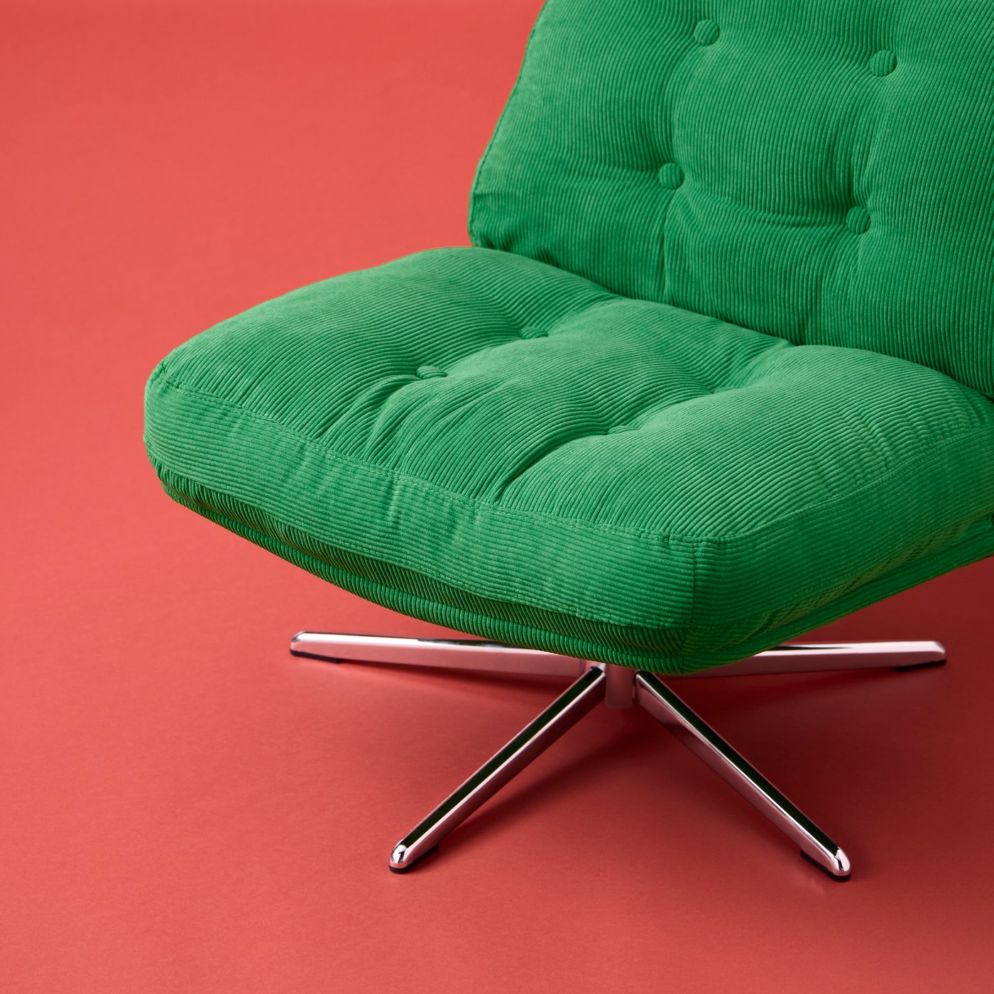 An empty DYVLINGE swivel easy chair in Kelinge green, corduroy-type fabric placed alone on an orange-red surface.