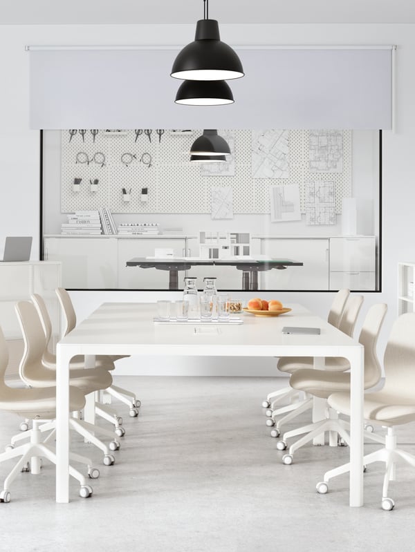 A meeting room with a white wall containing a large white table. A row of black SKURUP pendant lamps hang from the ceiling.