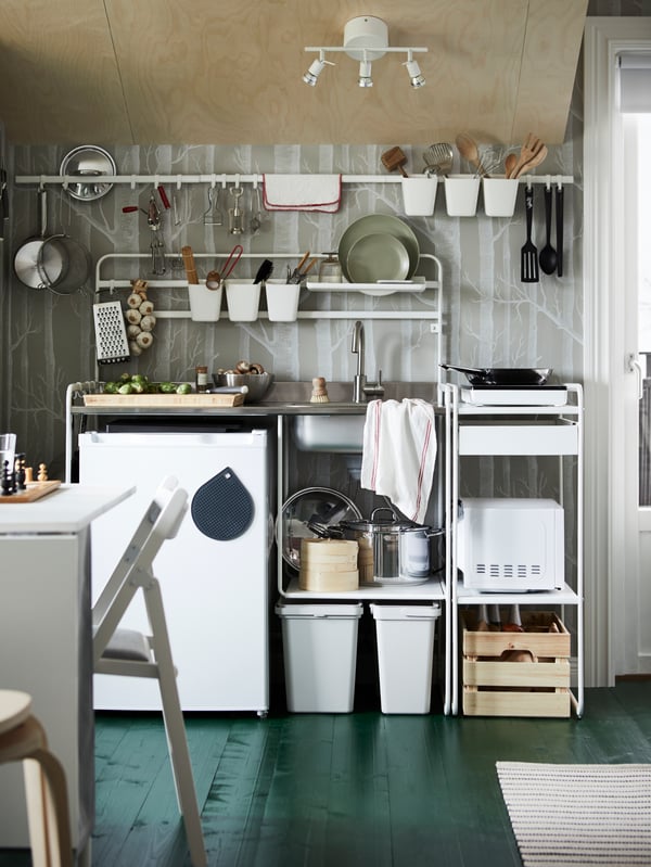 A SUNNERSTA unit kitchen against a grey wall with rails holding utensils, plates, and saucepans and a frying pan on the hob.