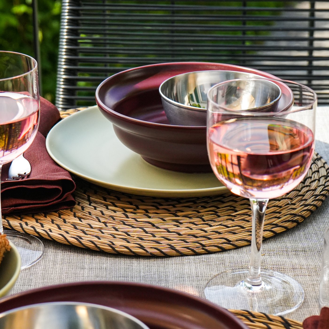 Gedeckter Tisch mit Roséweingläsern, dunklem Geschirr auf Bast-Platzsets und Scheiben von dunklem Brot, ideal für eine gemütliche Mahlzeit.