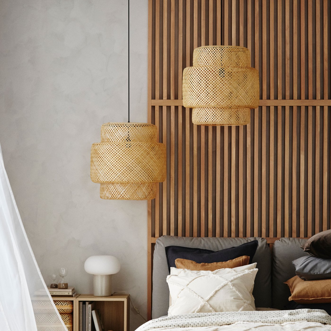 Two handmade bamboo SINNERLIG pendant lamps hang at different heights above a bed dressed in NYPONLUGGMAL bed linen.