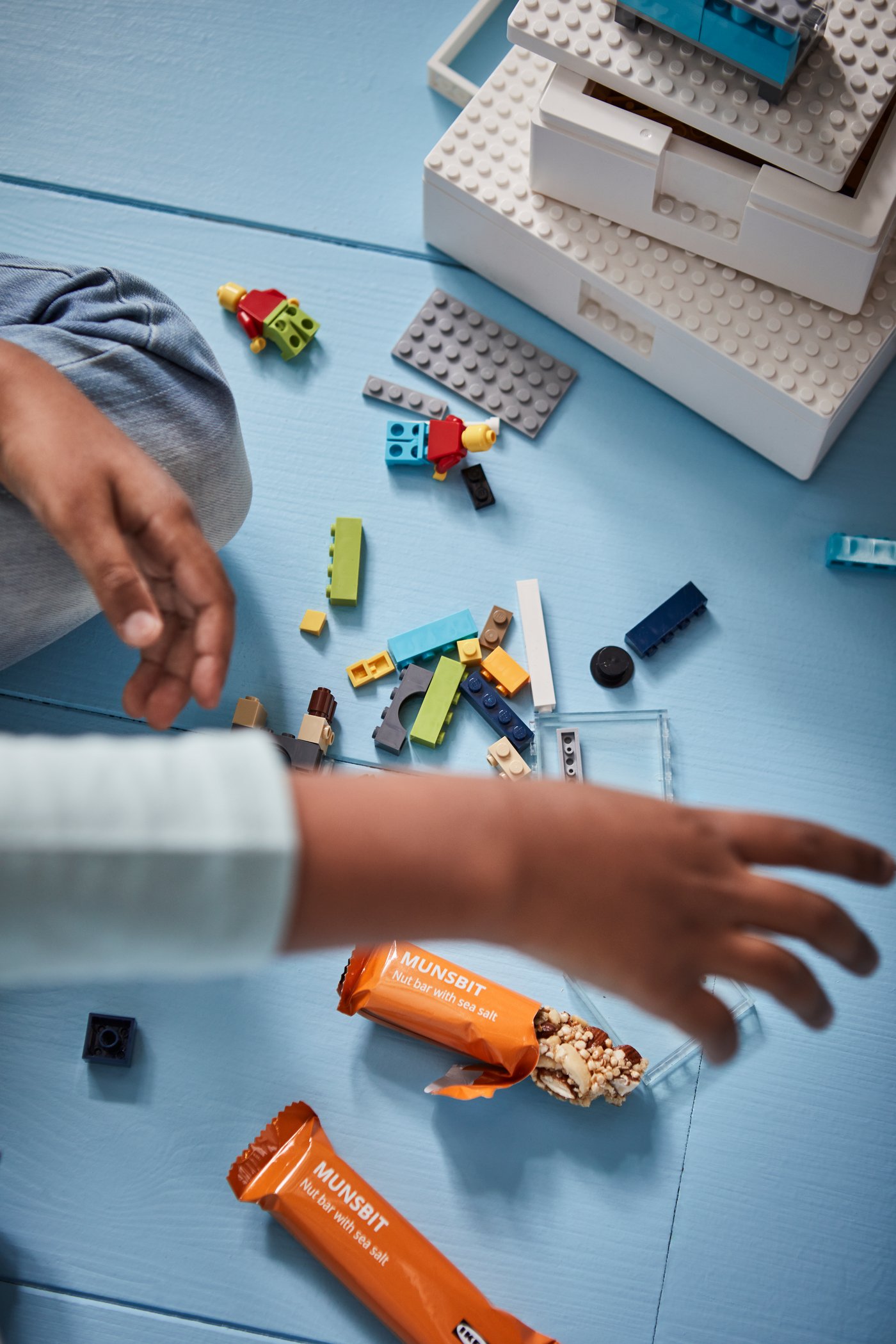 Unas manos de niño jugando con unos bloques de LEGO sobre una superficie celeste.