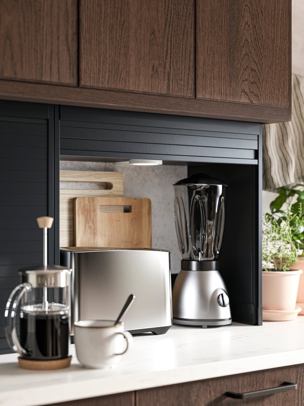 An open black TITTEBO tambour storage for small appliances showing a toaster, a blender and two chopping boards inside.