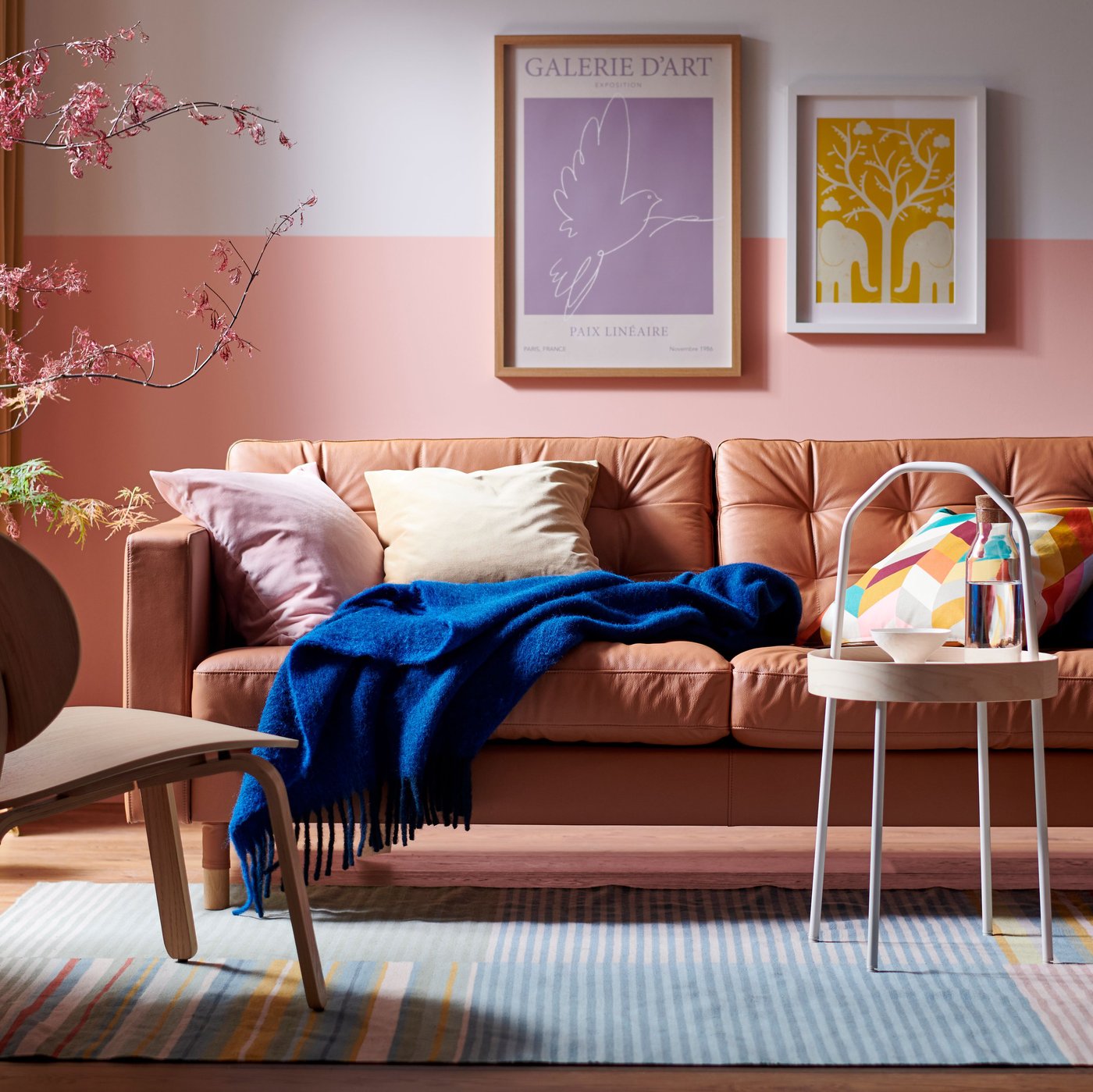 Ein LANDSKRONA-Sofa mit einer blauen KLIPPOXEL-Decke und zusätzlichen Kissen darauf und ein BURVIK-Beistelltisch stehen auf einem BUDDINGE-Teppich.