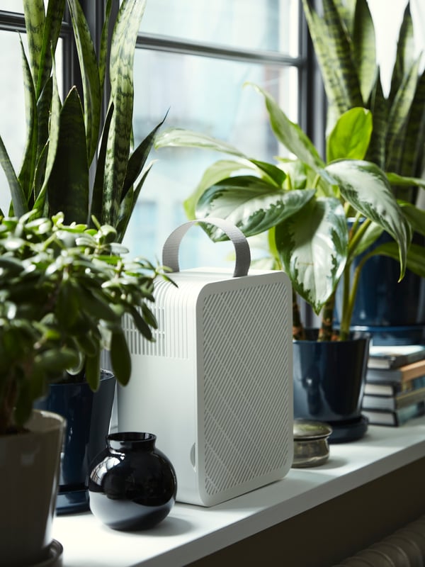 An UPPÅTVIND air purifier stands on a windowsill next to some plants in plant pots, books and other objects.